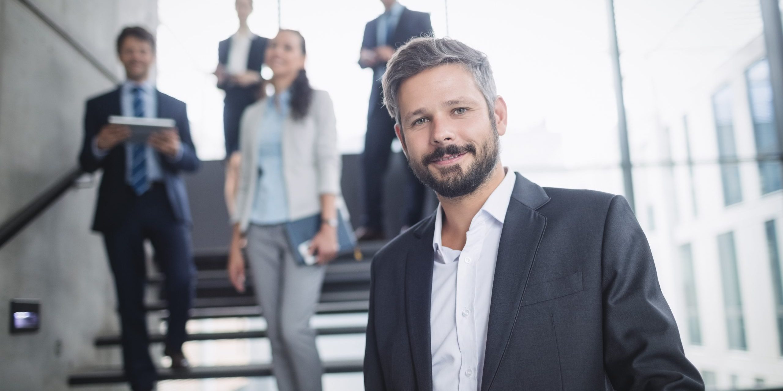 Photo of businessman with employees illustrates blog: "Taking Your Hiring to the Next Level in 2022"