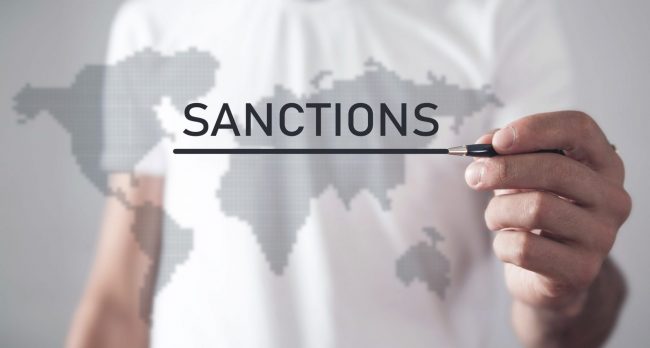 Photo of man writing the word "Sanctions" on a translucent map illustratees blog: "What Are OFAC Sanctions?"