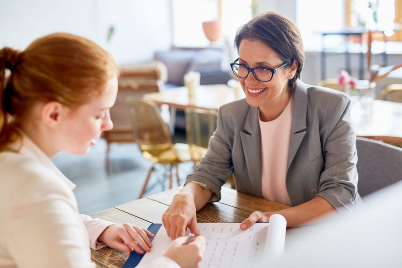 Photo of two women talking in office illustrates blog: "Adapting Your Hiring Processes and Policies to the Post-Pandemic World"