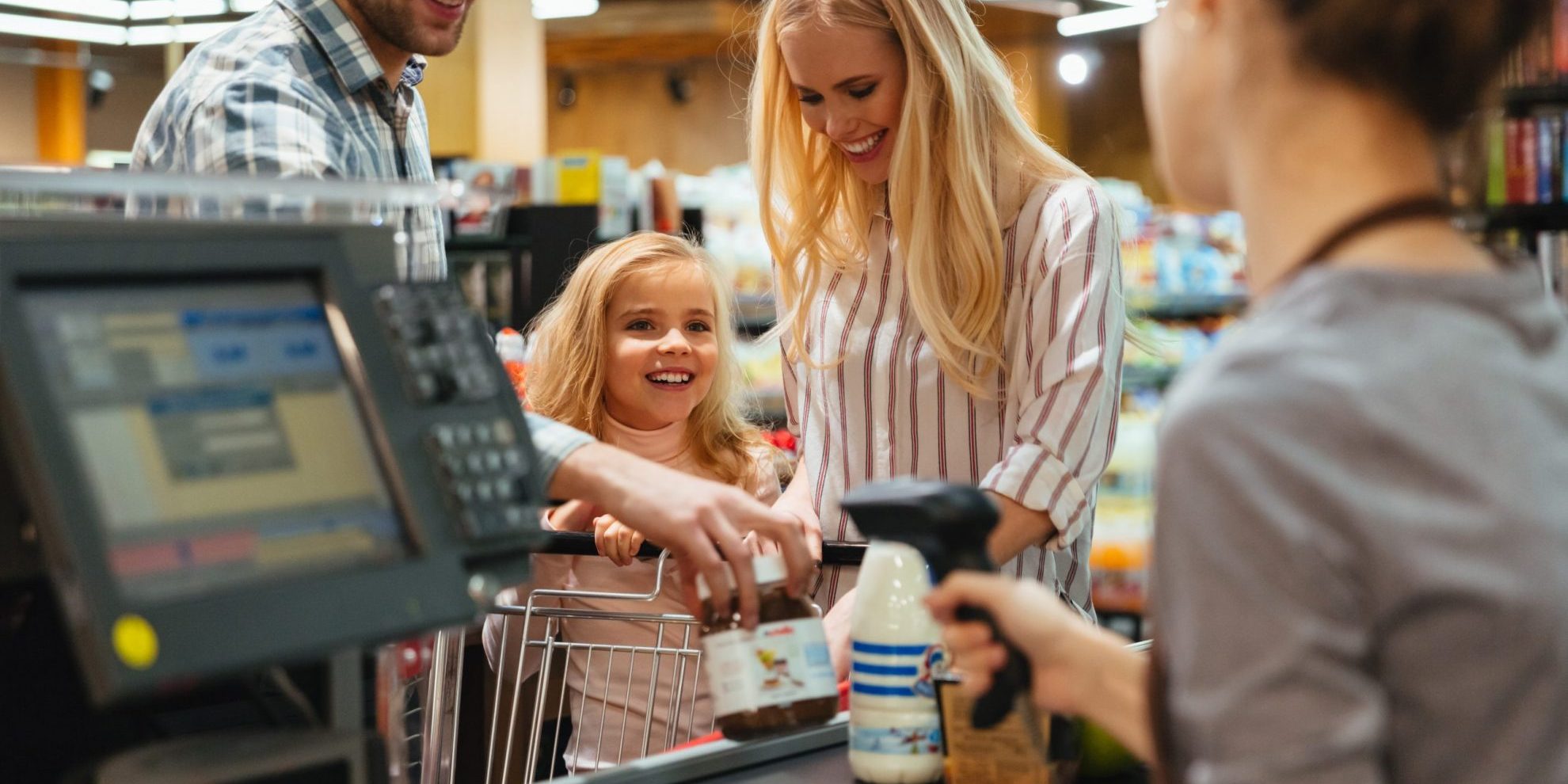 Photo of family at supermarket checkout counter with employee scanning items illustrates blog: "Background Checks for Retail Jobs: Here’s Why They Matter"