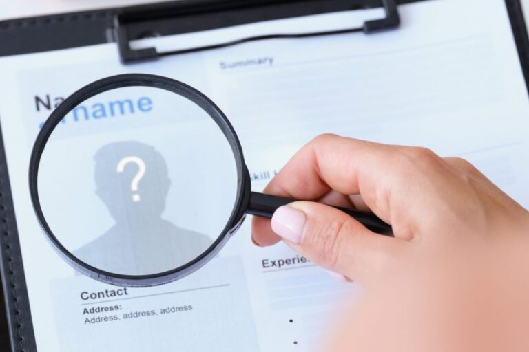 Photo of hand holding magnifying glass over resume illustrates blog: "Are Background Checks Accurate?"