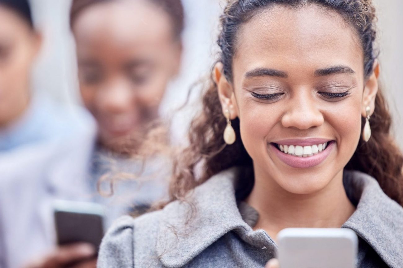 Photo of woman smiling looking at her smartphone illustrates blog: "What Is Candidate Experience and Why Is It Important?"