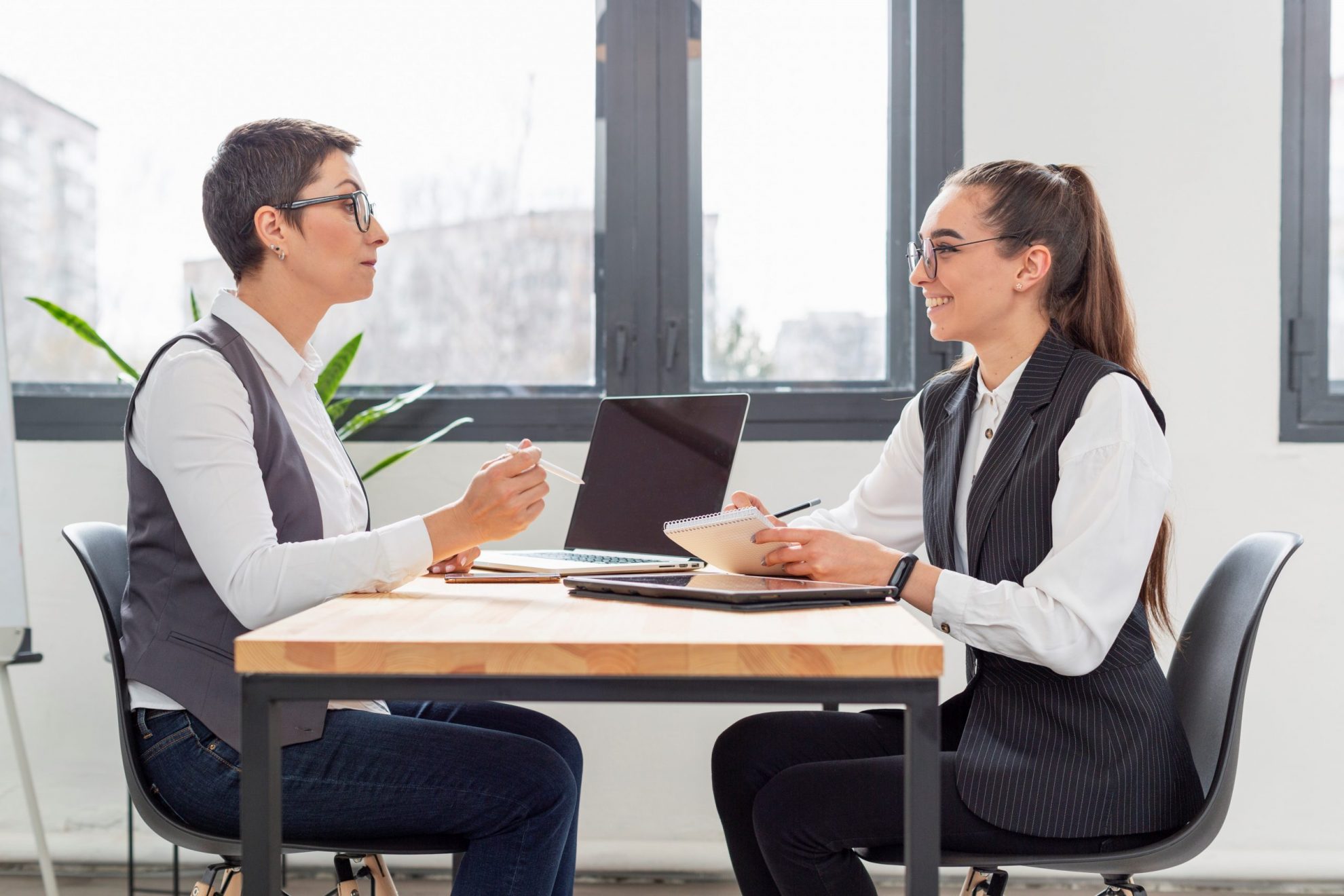 Two women sitting at desk talking illustrate blog "How to Use Active Listening When Conducting a Job Interview"