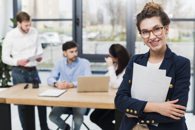 Woman in business attire with people sitting at desk in the background illustrates blog "Will a Background Check Show All My Jobs?"