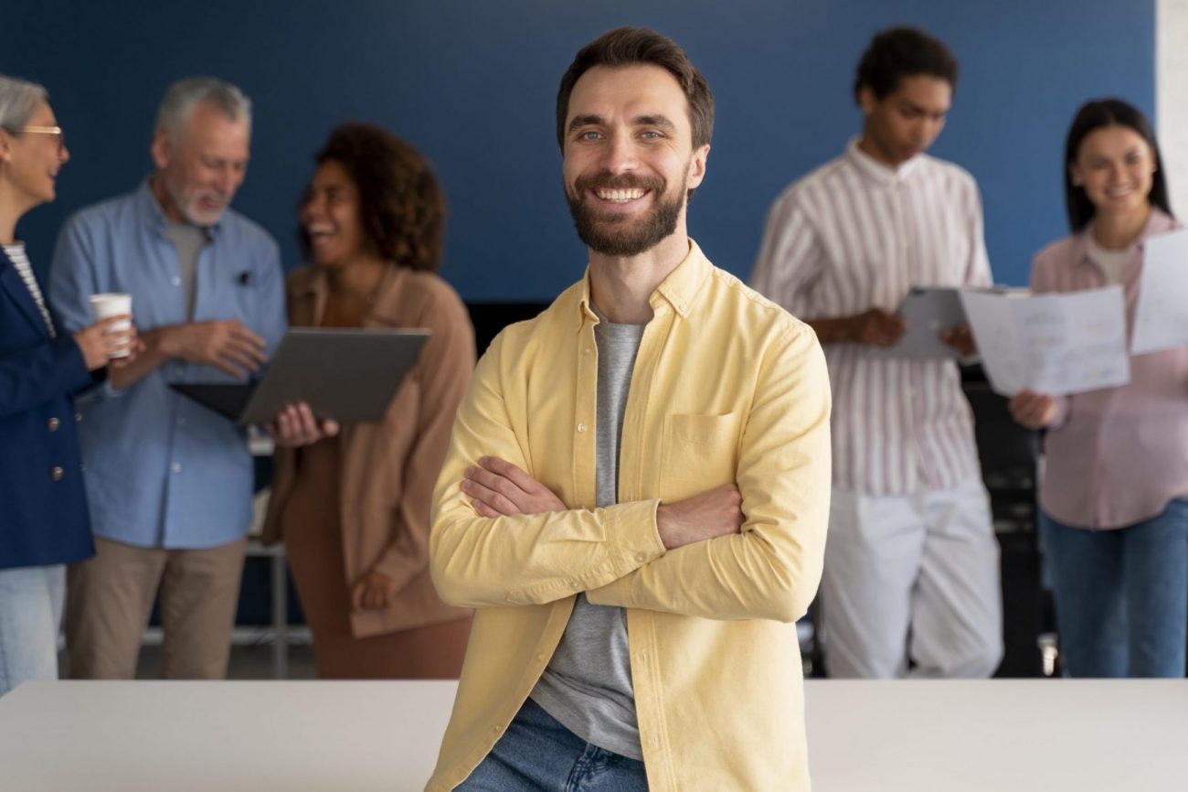 employer-employee-fp Man sitting on desk with people in the background illustrates blog "When To Run Background Checks?"