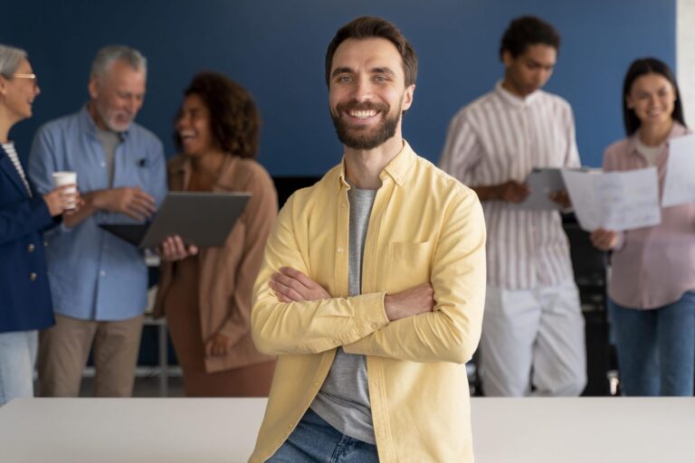 Man sitting on desk with people in the background illustrates blog "When To Run Background Checks?"